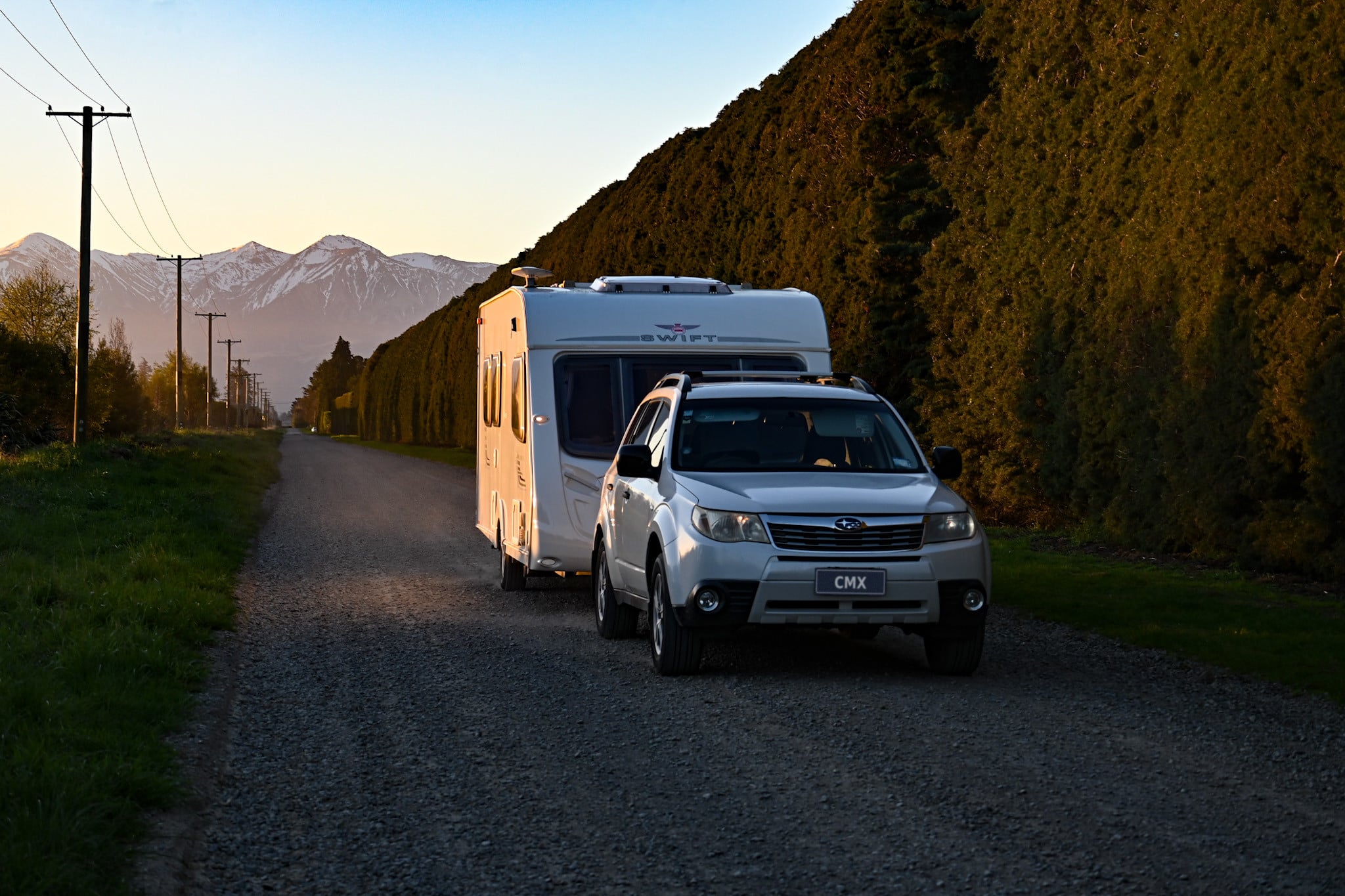 Car towing a caravan along a gravel road towards the Southern Alps in the evening light
